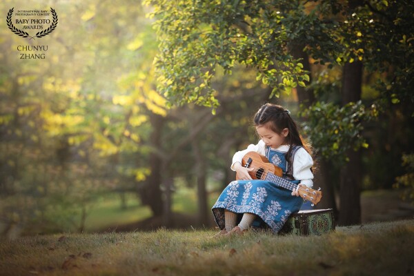 Autumn is coming! In the warm sunshine, a cute little girl is sitting in the forest learning to play the guitar，she is so dedicated and focused!