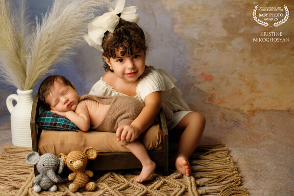 A tender sibling portrait, capturing the joy of a sister beside her peacefully sleeping newborn brot...