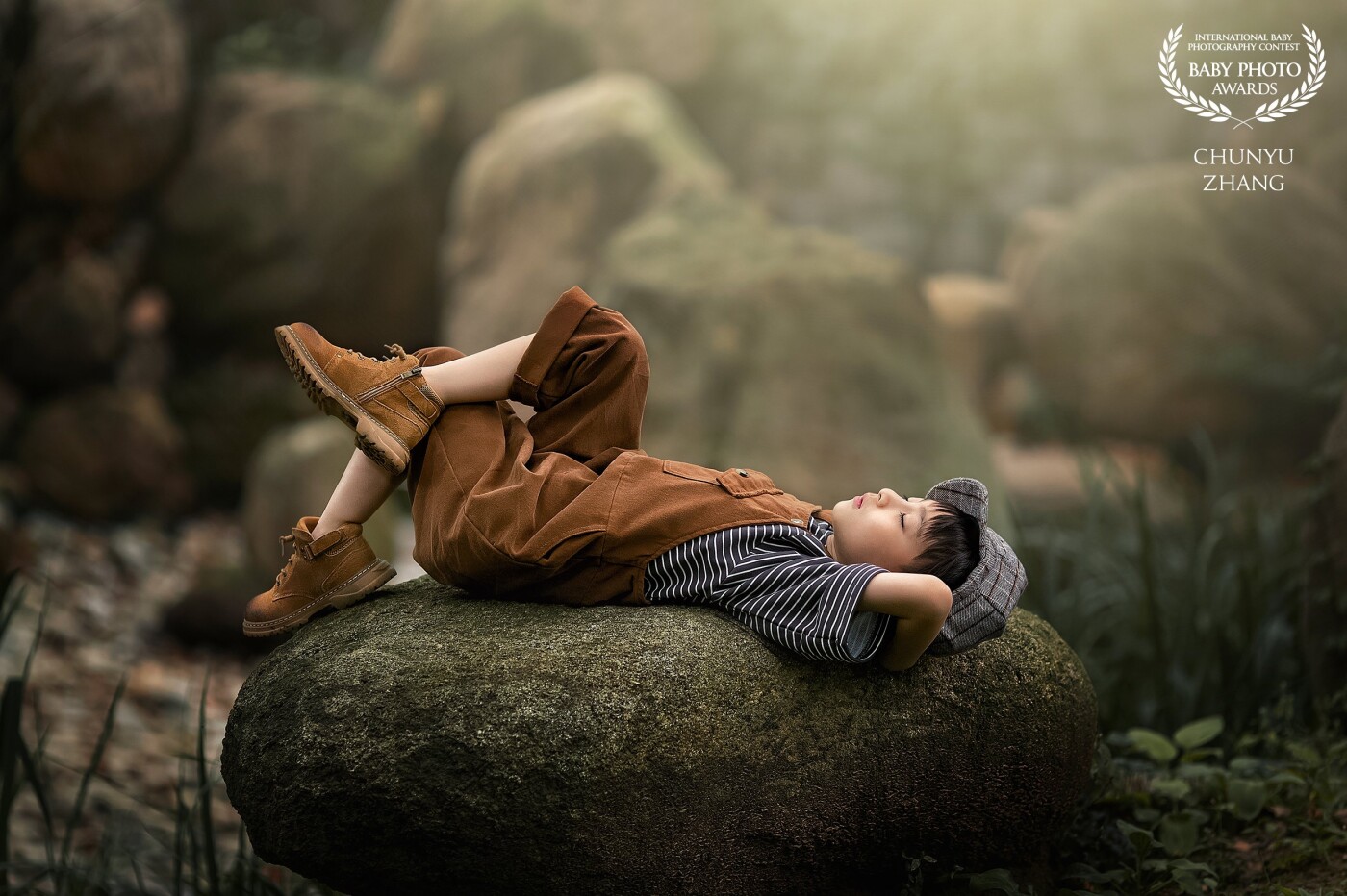 The little boy fell asleep in the afternoon sun,  beside a river and on a huge rock. He really enjoys this moment with nature. Here he could enjoy the sunshine, the breeze, the songs sang by the birds, what a wonderful day!