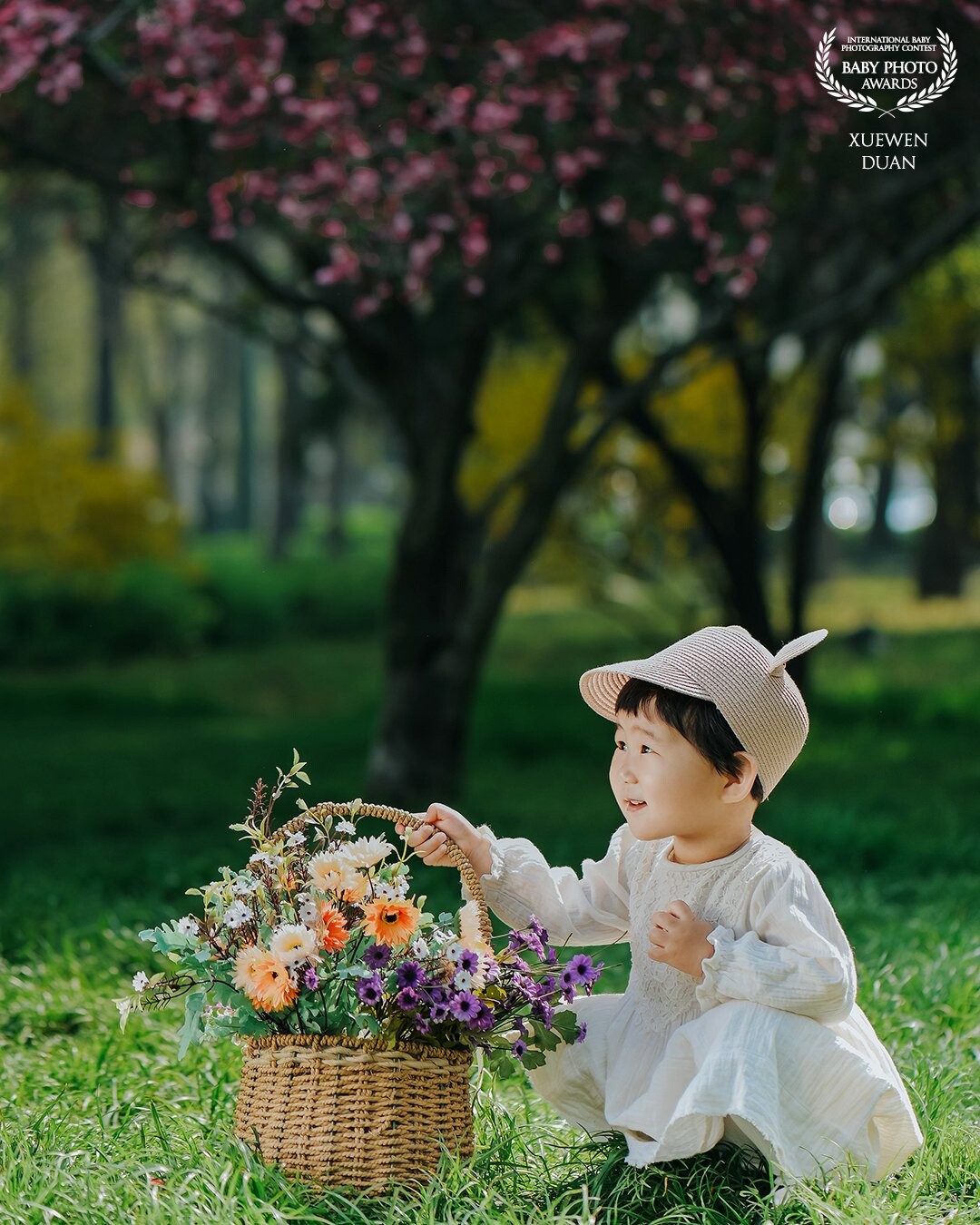 The day we took pictures of Miya, it was the season of travel. There were many people on the lawn. The morning sun came down and passed through the treetops. Miya held a beautiful flower basket and looked up and smiled. It was very beautiful.