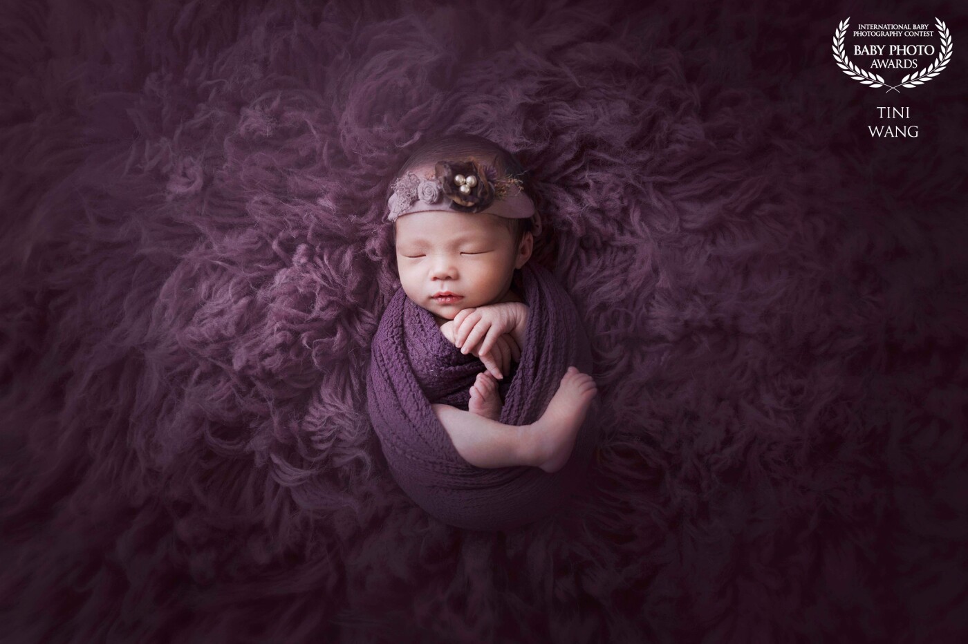 My baby client’s mother adores pink and purple, so I used a purple rug for the background to not only add color, but a soft texture to the photo. The swaddle blanket is a similar shade of purple that keeps my little client comfy and cozy. The pearl headband adorns her head to emphasize the delicate newborn.