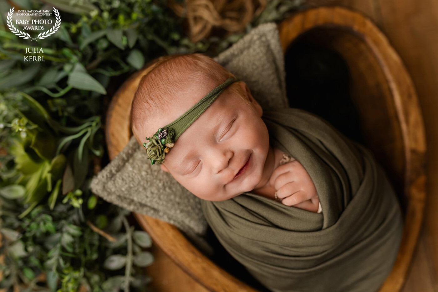 A newborn babygirl peacefully sleeps in a heart-shaped bowl. Her angel-smile radiates a sense of cosiness and warmth.