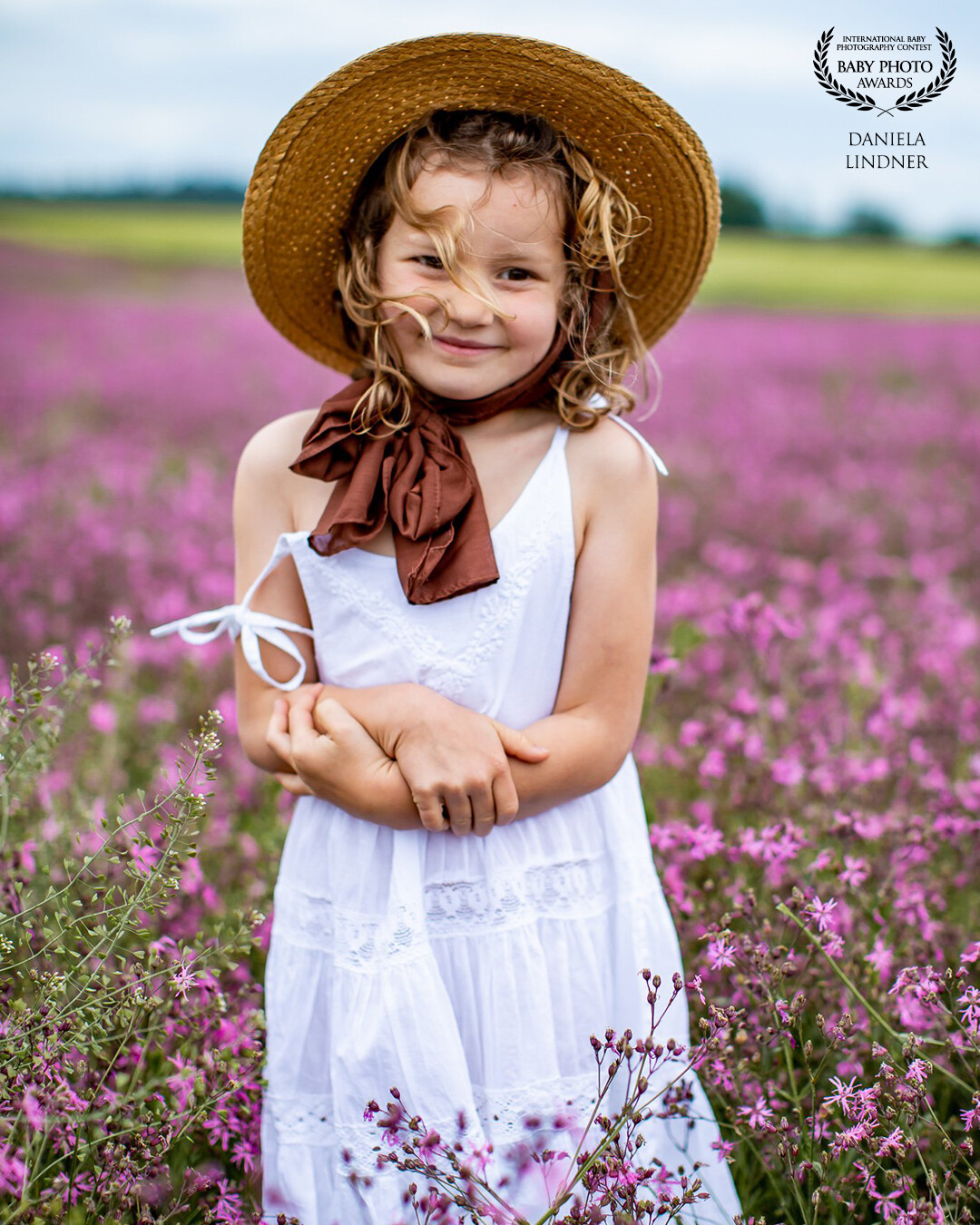 In an enchanting field of flowers blooming in soft shades of purple, stands a girl whose smile reflects the beauty of nature. The wind plays with her hair, which blows around her face in a harmonious dance. Her eyes shine with joy and lightheartedness.