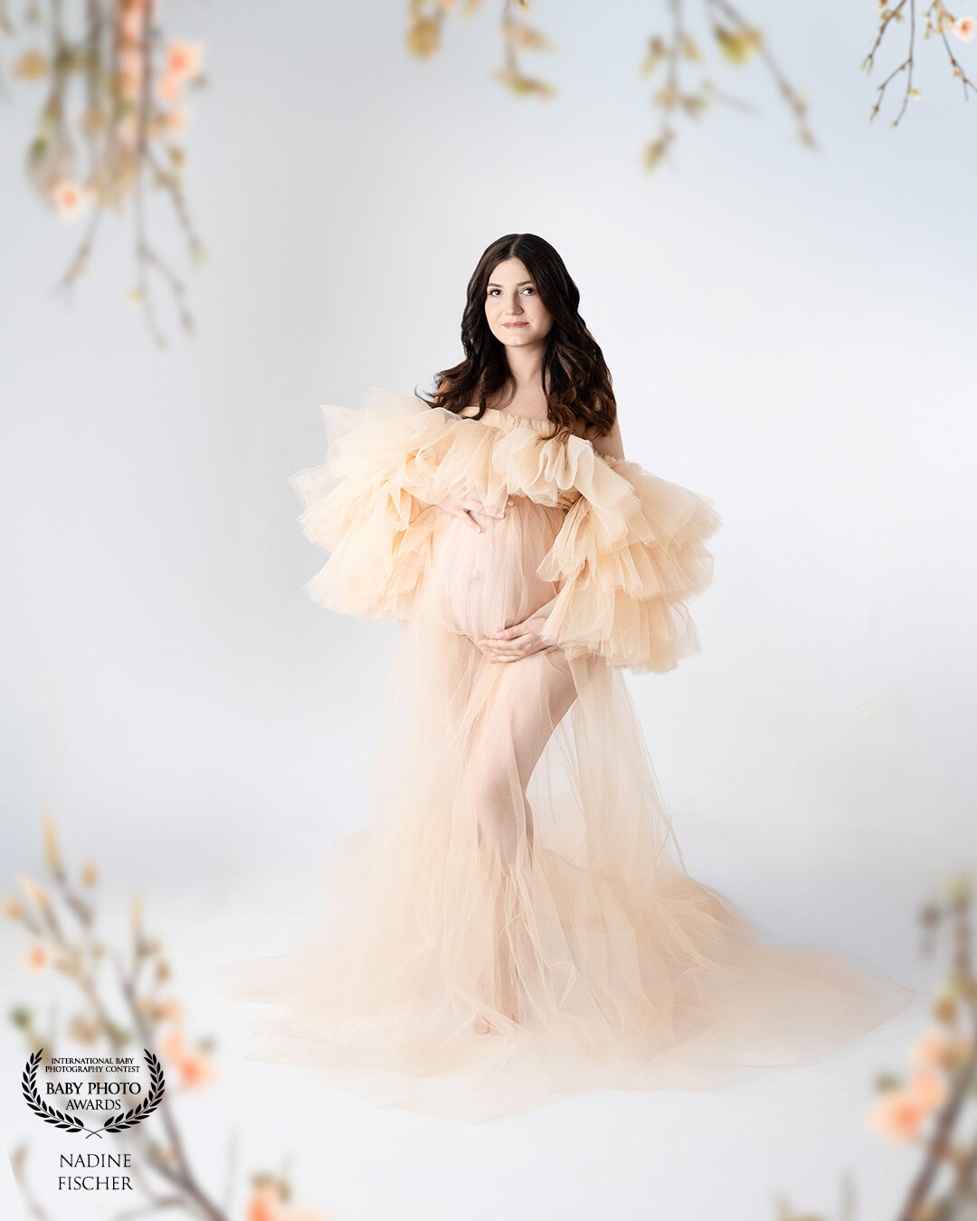 Title: "Spring Within"<br />
<br />
Framed by delicate blossoms, this maternity portrait radiates softness and renewal. The mother-to-be stands in a cloud of peach-hued tulle, embodying grace, hope, and new beginnings. Her gentle gaze and the pastel tones evoke the quiet beauty of spring and the anticipation of life.