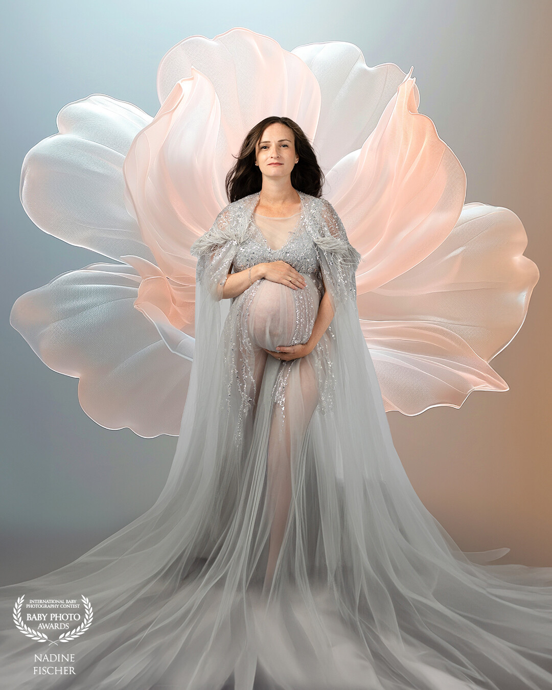 Title: "Blossoming Life"<br />
<br />
This portrait celebrates the strength and serenity of motherhood, with the expecting woman enveloped in flowing fabric that echoes the soft petals blooming behind her. The flower serves as a metaphor for new life, transformation, and natural beauty. Light and texture merge to create a timeless, ethereal atmosphere.