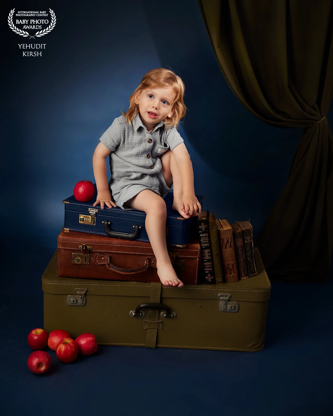 A dreamy, storybook-like atmosphere surrounds the young boy perched atop a stack of vintage suitcases. With a curious, thoughtful gaze and golden locks that frame his face, he seems like a little traveler from another time โ caught in a quiet moment between adventures. The deep blue background, old books, and scattered red apples evoke a sense of nostalgia and quiet wonder, as though he's stepped out of a timeless fairytale. Thereโs warmth in the scene, a blend of imagination and stillness โ inviting the viewer to pause, breathe, and dream alongside him.