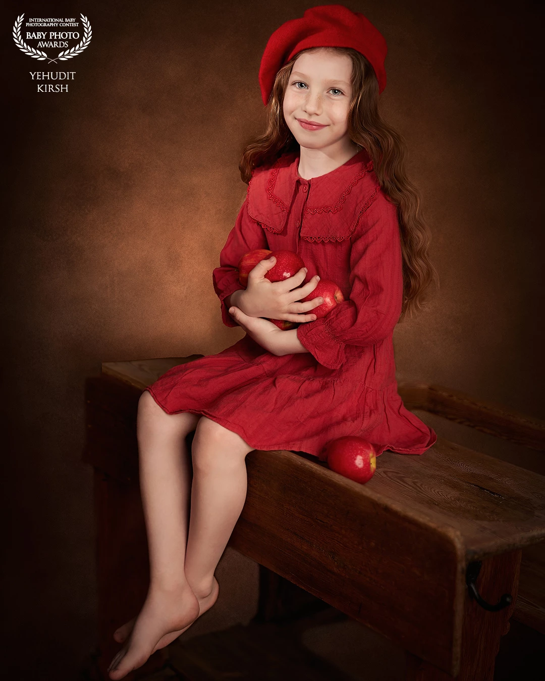 Bathed in warm, painterly tones, the scene feels like a frame from a timeless fairytale. A young girl, dressed in deep red from head to toe, sits gracefully on a rustic wooden bench. Her gentle smile and serene gaze evoke a quiet confidence, while her arms cradle a handful of red apples โ as if guarding a precious secret. The rich textures of her dress, beret, and flowing hair harmonize with the earthy background, creating a soft, nostalgic mood. This portrait captures more than a moment โ it tells a story of innocence, warmth, and quiet magic.