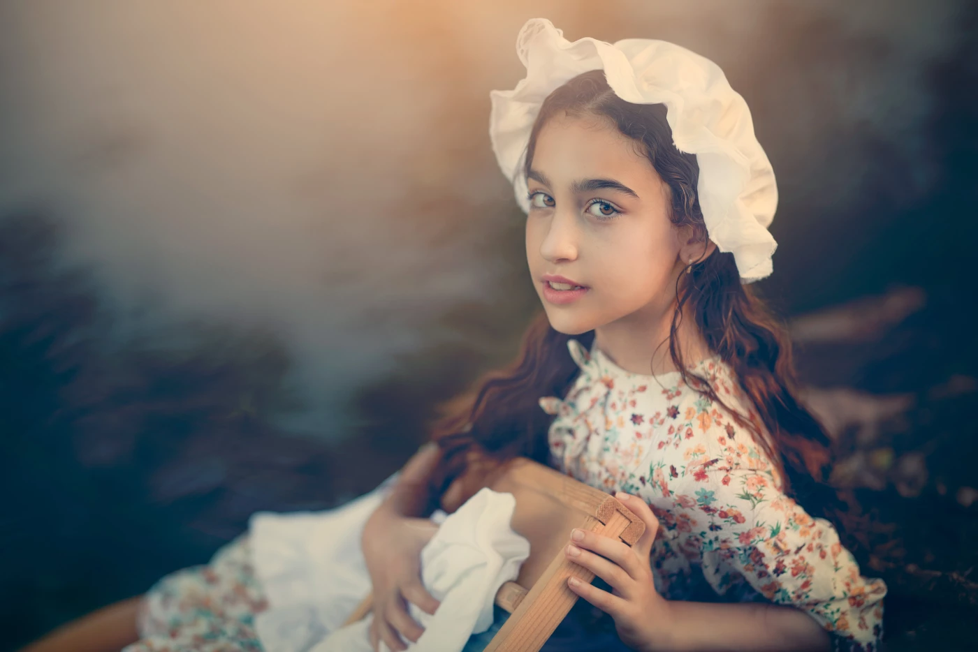 A young girl, dressed in vintage attire, kneels by the stream as she washes clothes by hand. The sce...