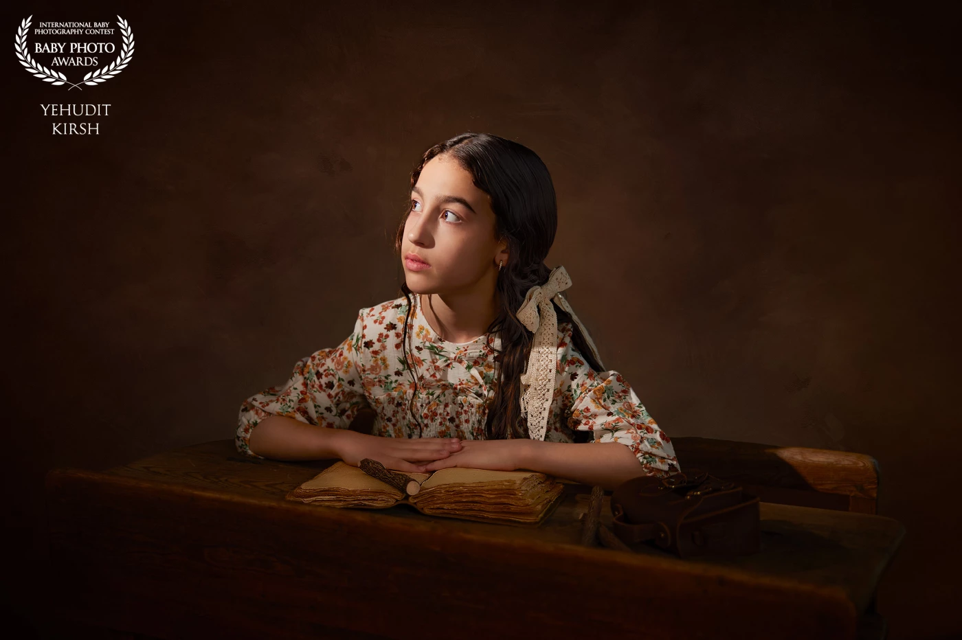 A young girl sits at an old wooden desk, bathed in a beam of dramatic light that cuts through the dim, earthy-toned room. Her delicate floral dress and ribbon-tied hair evoke a timeless, vintage charm. In front of her lies an aged, weathered journal — its pages whispering forgotten stories. Her gaze, thoughtful and distant, captures a quiet moment of wonder and reflection, as though she’s caught between memory and imagination.