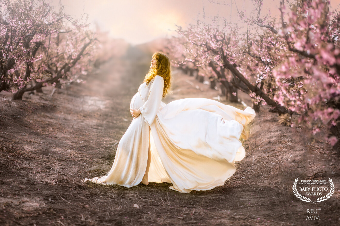 A stunning pregnant woman poses in a dress that seamlessly blends with the surrounding pink peach field, creating a serene and ethereal atmosphere that captures the beauty and magic of motherhood.