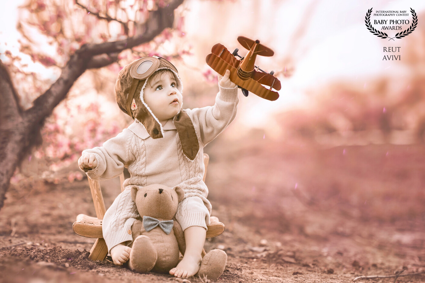 In a peach field with pink flowers, a one-year-old boy joyfully flies his airplane, feeling the thrill of adventure as he explores the magical world around him.
